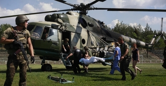 Ukrajinští vojáci odvážejí vrtulníkem zraněného kamaráda.