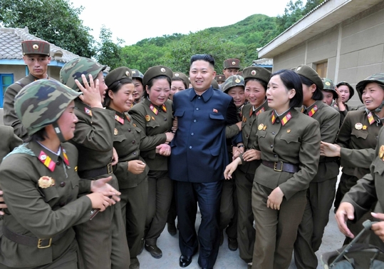 Šťastný Kim objímaný mladicemi v uniformách.