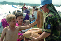 Uprchlíci ze Srebrenice. Nizozemští příslušníci UNPROFOR rozdávají chléb bosenským dětem na letišti v Tuzle. Červenec 1995.
